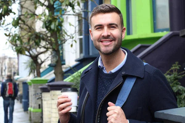 Sokakta elinde kağıt bardak kahveyle ceketli yakışıklı bir gencin yakın plan portresi.