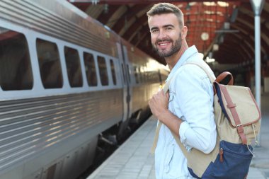 Tren istasyonunda sıradan kıyafetler giymiş yakışıklı bir gencin yakın plan portresi.