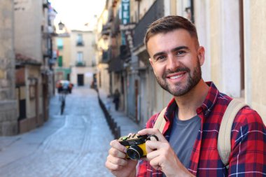 Eski şehir caddesinde sırt çantalı ve klasik kameralı yakışıklı bir gencin yakın plan portresi.