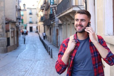 Sırt çantalı yakışıklı genç adamın eski şehir caddesinde telefonla konuşurken yakın plan portresi.