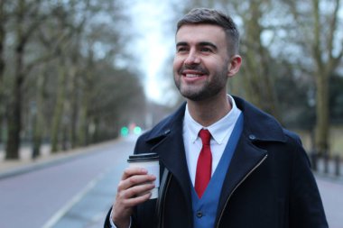 Takım elbiseli ve ceketli yakışıklı genç işadamının kağıt bardak kahveyle yakın plan portresi.