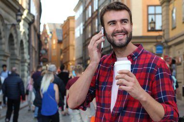 Sokakta elinde kağıt kahve olan yakışıklı bir gencin yakın plan portresi.