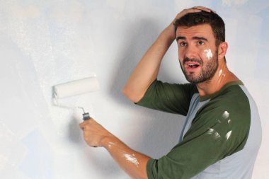 close-up portrait of handsome young man painting wall with rolling brush at home