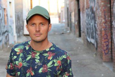 Çiçek desenli ve şapkalı tişörtlü yakışıklı genç adamın yakın plan portresi.