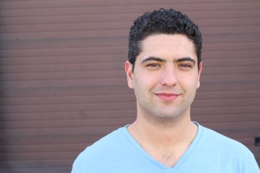 close-up portrait of handsome young man in blue t-shirt in front of brown wall