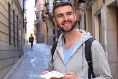Sırt çantalı ve kitaplı yakışıklı genç adamın şehir sokaklarındaki yakın plan portresi.