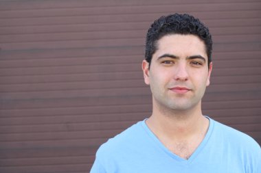 close-up portrait of handsome young man in blue t-shirt in front of brown wall