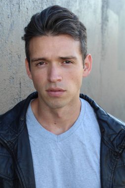 Gri duvarın önünde sıradan giyinmiş yakışıklı bir gencin yakın plan portresi.