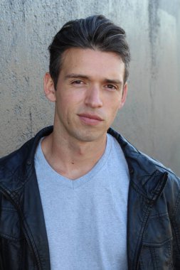 Gri duvarın önünde sıradan giyinmiş yakışıklı bir gencin yakın plan portresi.