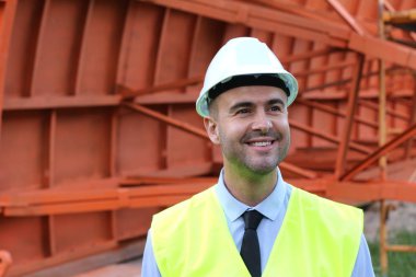 İnşaat alanında koruyucu yelek giymiş yakışıklı bir mimarın yakın plan portresi.