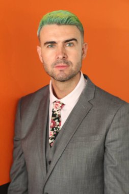 Turuncu arka planda duran yeşil saçlı zarif yakışıklı adam.