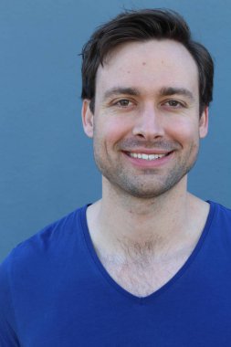 Mavi duvarın önünde sıradan giyinmiş yakışıklı bir gencin yakın plan portresi.