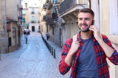 Sırt çantalı yakışıklı genç adamın eski şehir caddesinde telefonla konuşurken yakın plan portresi.