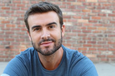 Tuğla duvarın önündeki mavi tişörtlü yakışıklı genç adamın yakın plan portresi.