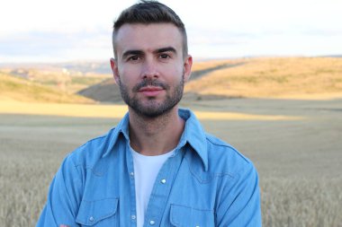 Genç adam buğday tarlasında dururken gülümsüyor. 