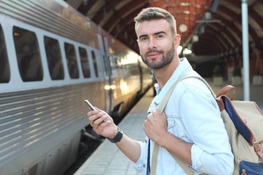 Yakından bakınca, tren istasyonunda akıllı telefonlu sıradan giysili yakışıklı bir gencin portresi.