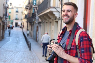 Eski şehir sokaklarında sırt çantalı ve DSR kameralı yakışıklı genç adamın yakın plan portresi.