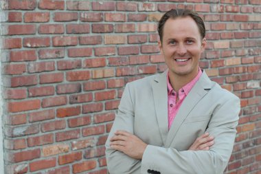 Tuğla duvarın önünde bej takım elbiseli yakışıklı genç işadamının yakın plan portresi.