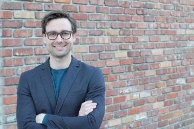 Tuğla duvarın önünde yakışıklı genç işadamının yakın plan çekimi.