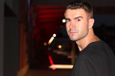 Geceleri sokakta siyah tişörtlü yakışıklı bir adamın yakın plan portresi.