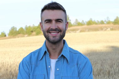 Genç adam buğday tarlasında dururken gülümsüyor. 