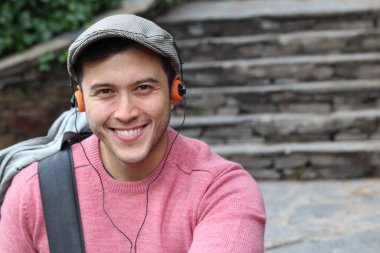 Yakından çekilmiş bir portre, günlük giysiler içindeki yakışıklı genç adam klasik kulaklıklarla müzik dinliyor ve şehir sokaklarında oyuncu.