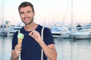 Gün batımında yatların önünde limanda dondurma yiyen şık elbiseli yakışıklı bir gencin yakın plan portresi. 