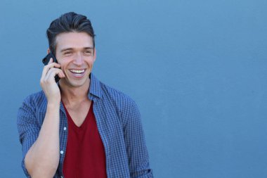 Mavi duvarın önünde telefonla konuşan yakışıklı bir gencin yakın plan portresi.