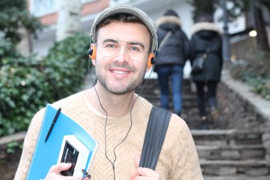 Yakından çekilmiş bir portre, günlük giysiler içindeki yakışıklı genç adam klasik kulaklıklarla müzik dinliyor ve şehir sokaklarında oyuncu.