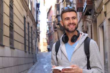 Sırt çantalı ve kitaplı yakışıklı genç adamın şehir sokaklarındaki yakın plan portresi.