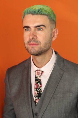 Turuncu arka planda duran yeşil saçlı zarif yakışıklı adam.