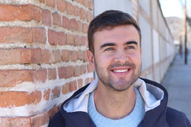 Yakından bakınca, tuğla duvara yaslanmış, günlük giysiler içinde yakışıklı bir gencin portresi.