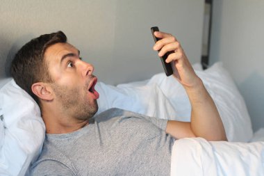 Evdeki yatakta akıllı telefon kullanan yakışıklı bir gencin yakın plan portresi.