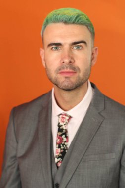 Turuncu arka planda duran yeşil saçlı zarif yakışıklı adam.