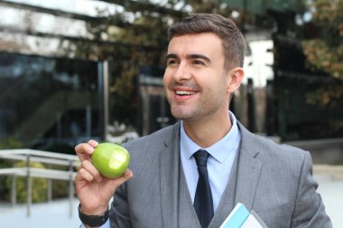close-up portrait of handsome young businessman in suit eating green apple on street clipart