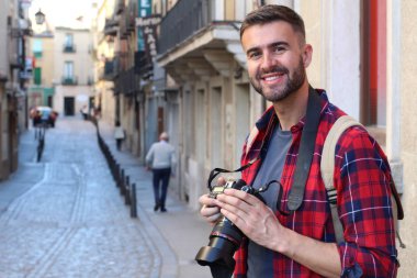 Eski şehir sokaklarında sırt çantalı ve DSR kameralı yakışıklı genç adamın yakın plan portresi.
