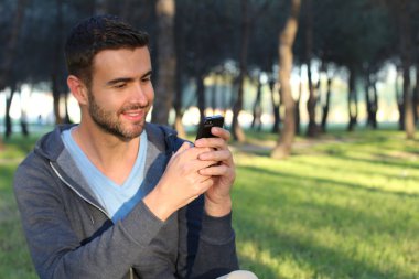 Parkta akıllı telefon kullanan yakışıklı bir gencin yakın plan portresi.