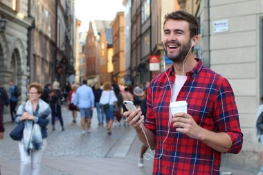 Sokakta elinde kağıt kahve olan yakışıklı bir gencin yakın plan portresi.