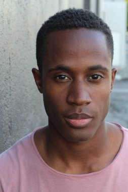 Gri duvarın önünde pembe tişörtlü yakışıklı genç adamın yakın plan portresi.