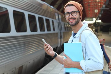 Yakından bakınca, tren istasyonunda akıllı telefonlu sıradan giysili yakışıklı bir gencin portresi.