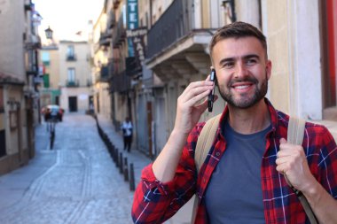 Sırt çantalı yakışıklı genç adamın eski şehir caddesinde telefonla konuşurken yakın plan portresi.