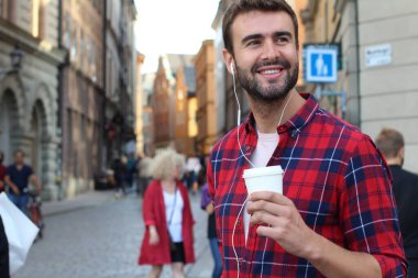 Sokakta elinde kağıt kahve olan yakışıklı bir gencin yakın plan portresi.