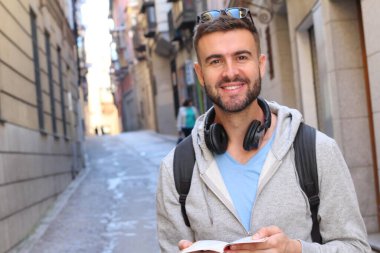 Sırt çantalı ve kitaplı yakışıklı genç adamın şehir sokaklarındaki yakın plan portresi.