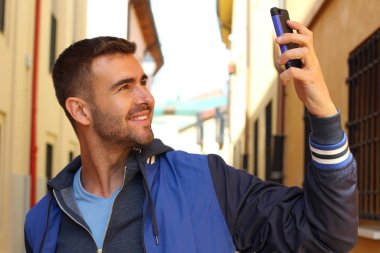 Sokakta akıllı telefon kullanarak günlük kıyafetler giyen yakışıklı genç adamın yakın plan portresi.