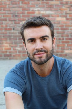 Tuğla duvarın önündeki mavi tişörtlü yakışıklı genç adamın yakın plan portresi.