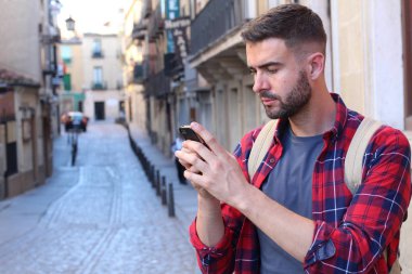 Eski şehir caddesinde akıllı telefon kullanan sırt çantalı yakışıklı bir gencin yakın plan portresi.