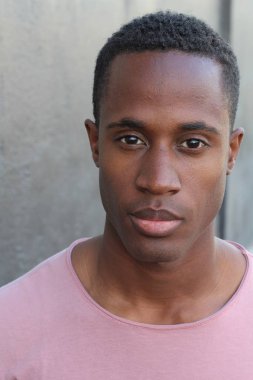 Gri duvarın önünde pembe tişörtlü yakışıklı genç adamın yakın plan portresi.