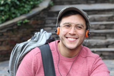 Yakından çekilmiş bir portre, günlük giysiler içindeki yakışıklı genç adam klasik kulaklıklarla müzik dinliyor ve şehir sokaklarında oyuncu.