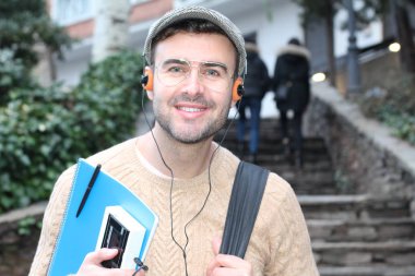 Yakından çekilmiş bir portre, günlük giysiler içindeki yakışıklı genç adam klasik kulaklıklarla müzik dinliyor ve şehir sokaklarında oyuncu.