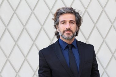 Duvarın önündeki siyah takım elbiseli yakışıklı iş adamının yakın plan fotoğrafı.